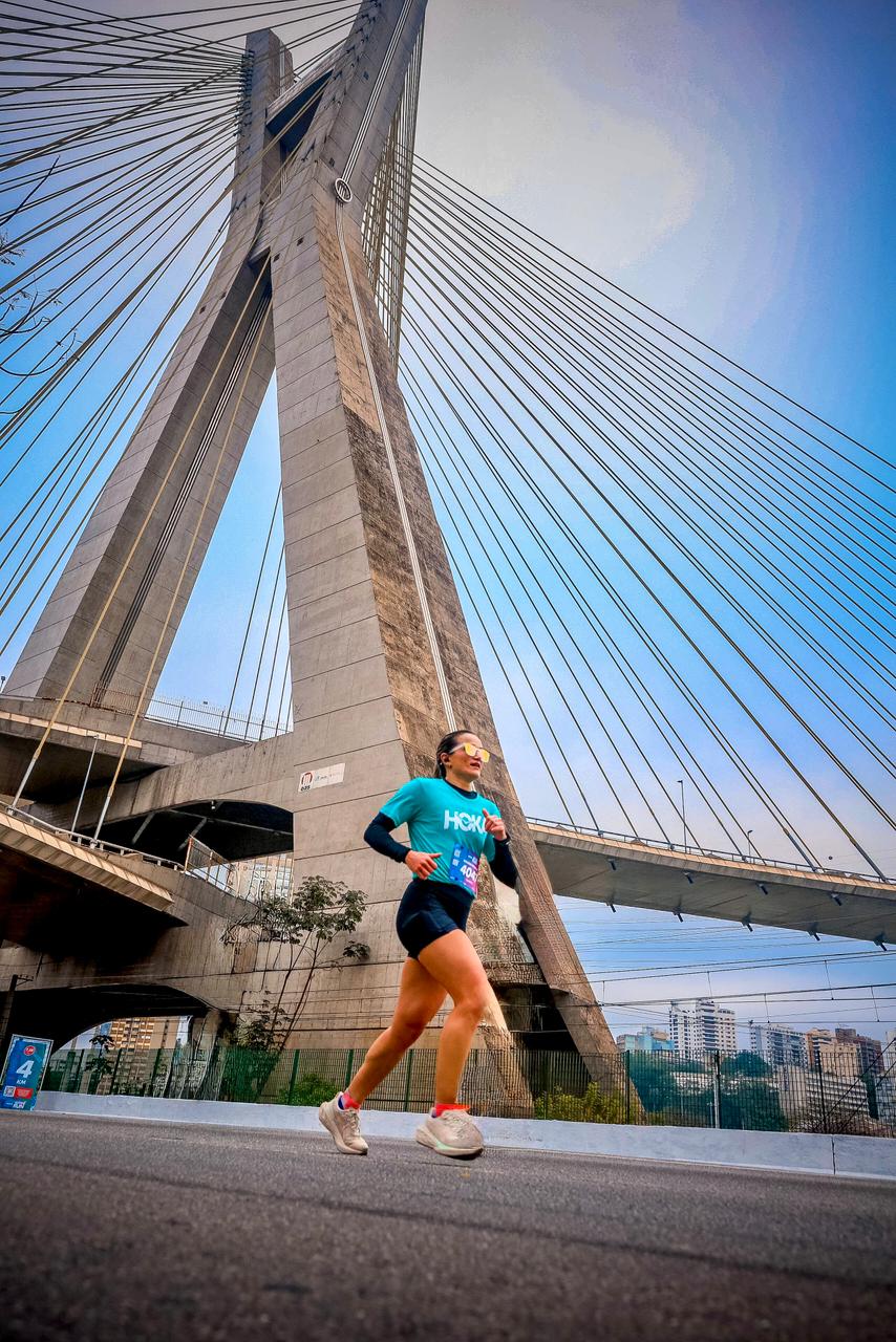Kátia Wolff correndo em frente à ponte estaiada, com destaque para a imponência da estrutura