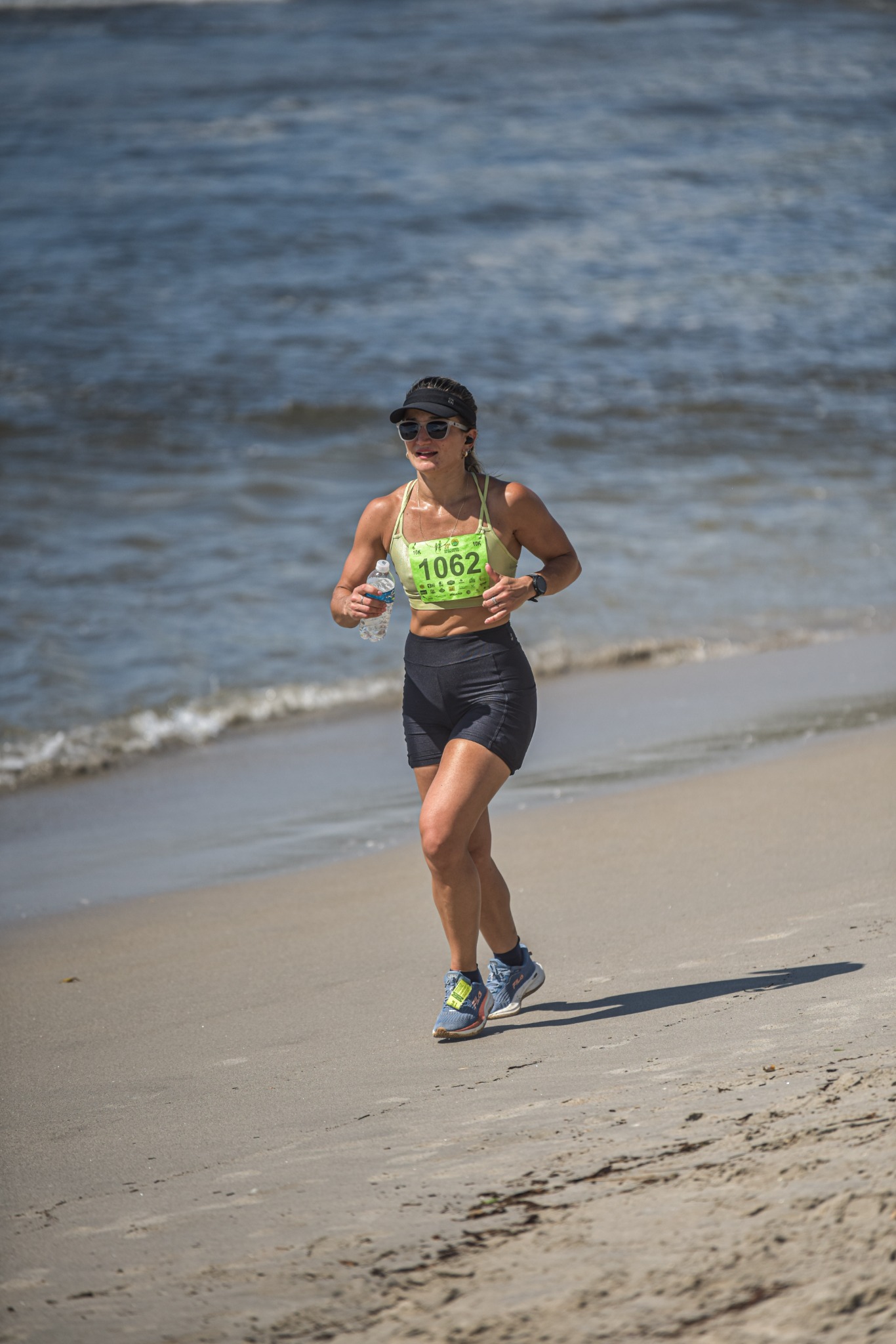 Corredora em prova de 10 km na beira da praia, com garrafa de água na mão
