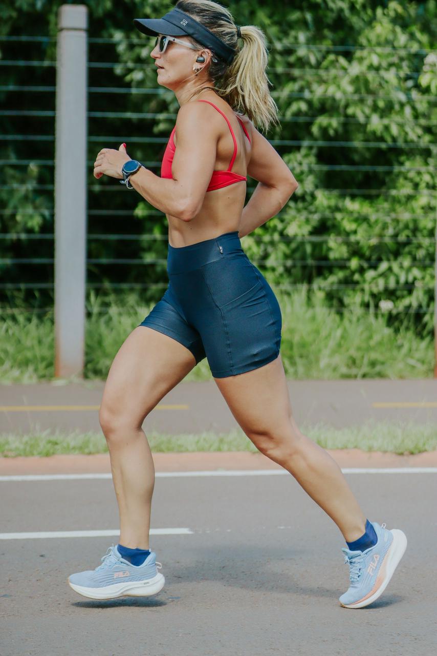 Corredora de perfil em passada firme durante treino em pista de asfalto